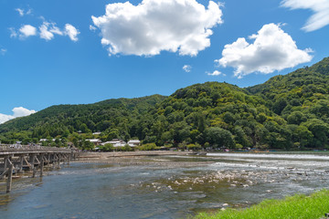 Fototapeta na wymiar Togetsu-kyo bridge over katsuragawa river with colourful forest mountain background in Arashiyama district. Arashiyama is a nationally designated Historic Site and Place of Scenic Beauty. Kyoto, Japan