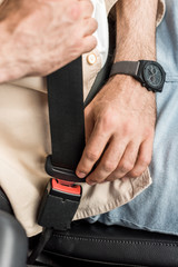cropped view of man fastening seat belt in car