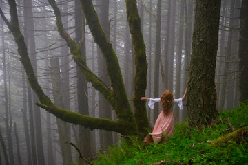 Woman lost in the woods. Red head woman in foggy forest near the tree covered with moss. Spring rainforest in Columbia River Gorge near Portland. Oregon. United States of America.