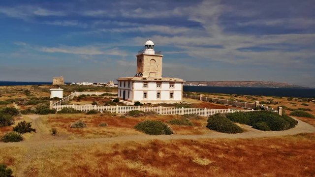 The beautiful lighthouse on the small romantic Spanish island Tabarca and in the background the village. The sun is shining and the Mediterranean is blue. Aerial drone 4k.