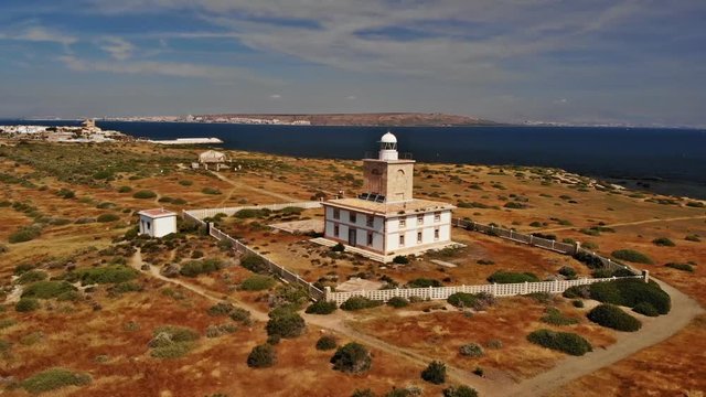 The beautiful lighthouse on the small romantic Spanish island Tabarca off the coast of Alicante. The sun is shining and the Mediterranean is blue. Semicircle Flight Aerial drone 4k.