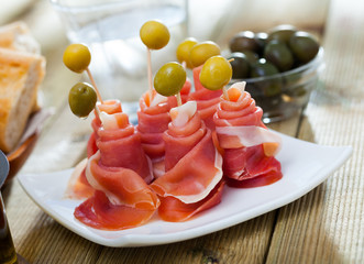 Rolled up dry-cured ham slices with olives