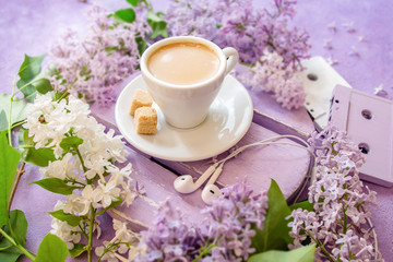 Obraz na płótnie Canvas Coffee with cream and cane sugar on a lilac table, surrounded by lilac flowers. Old music cassettes and headphones.