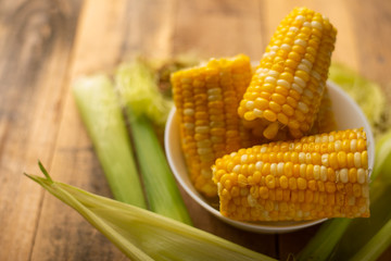 boiled corn cob in a plate with butter, on wooden textures and green stalks of corn, tasty homemade food, for a picnic