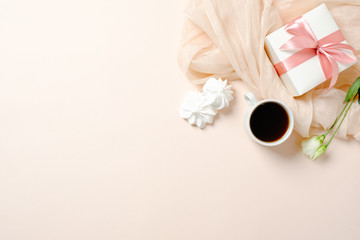 Flat lay home office desk. Female workspace with coffee cup, gift box, marshmallows and roses on pink background. Top view feminine background with copy space for text.