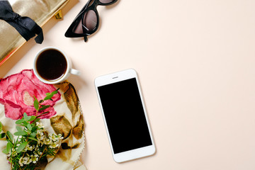 Flat lay home office desk. Female workspace with smartphone, pink scarf, golden accessories, coffee cup and sunglasses on pastel pink background. Top view feminine background with copy space for text.