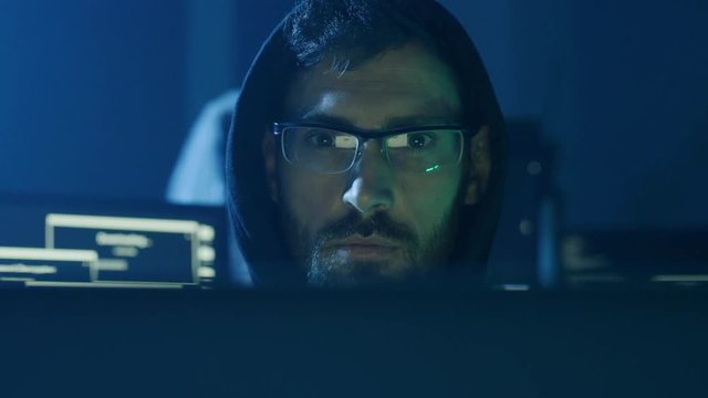 Portrait of concentrated programmer looking at computer interface sitting at desk. Young smart man working in software development office at night. Close-up view.