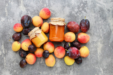 Peaches, plums and two jars with jam on gray stone background.