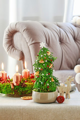 Christmas decoration in tree shape with moss, cinnamon sticks and rose hip and advent wreath on the table.