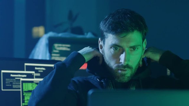 Concentrated programmer typing data codes on laptop looking at interface. Portrait of exhausted young man hiding face working in the office at night.