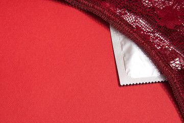 Red female lacy panties lie on a silver condom on a scarlet background