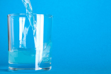 Blue carbonated liquid is poured into a glass from a bottle on a blue background with space for text