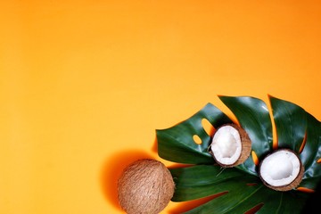 coconuts and tropical leaf of monstera plant with on orange background. Flat layer, top view, copy space. Healthy cooking. Creative concept of healthy eating. horizontal