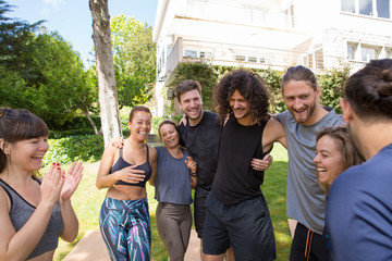 Happy friends having fun after yoga class in park. Group of people hugging each other, laughing and chatting. Joy and outdoor activity concept