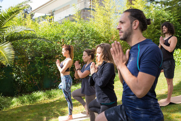 Serene people enjoying yoga class outdoors. Men and women in fitness apparels standing on grass in park and holding tree pose. Training in park concept