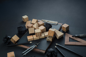 Ruined toy house with toy wooden blocks, pencils, rulers and copy space. Insurance and real estate risk concept on a dark background with copy space.