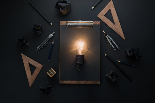Light bulb in black on black flat lay with architect tools, rulers and pencils. Idea for engineering, building or construction with copy space.