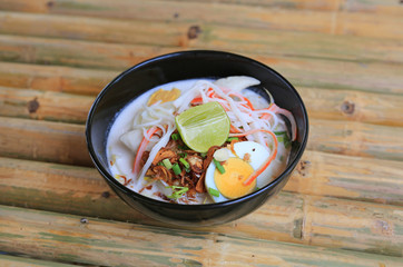 Noodle in coconut milk soup in bowl on bamboo wood table. Fusion Thai food.