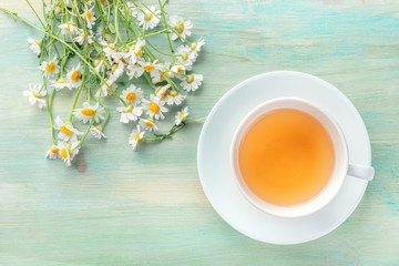 A cup of chamomile tea, shot from the top on a teal blue background with a bouquet of flowers and a...