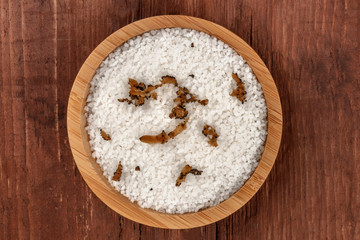 A closeup of a bowl of sea salt infused with truffle shavings, shot from the top on a dark rustic wooden background