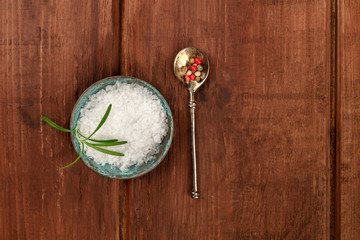 Fototapeta na wymiar Gourmet spices. Rosemary infused sea salt and a spoon with peppercorns, shot from the top on a dark rustic wooden background with a place for text