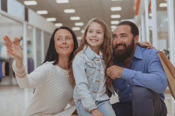 Beautiful woman pointing away at the shopping mall, enjoying shopping spree with her lovely family. Mature couple and their cute little girl shopping together. Consumerism, family activity concept