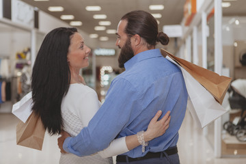 Obraz premium Rear view of a happy mature couple smiling at each other, hugging at the shopping mall. Loving husband and wife enjoying shopping spree at the mall. Love, anniversary, celebration concept