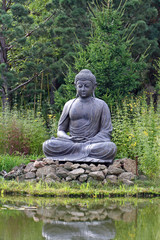 Buddha statue meditating in front of lake, in the nature