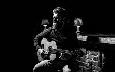 Play the guitar. Beard hipster man sitting in a pub. Guitars and strings. Bearded man playing guitar, holding an acoustic guitar in his hands. Bearded guitarist plays. Black and white