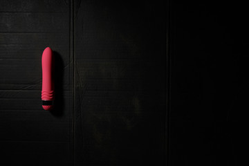 Simple pink dildo on dirty black background with hard light and shadows with copyspace.