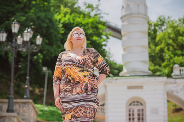 Fototapeta premium XXL woman walking on the city street at summer. Casual fashion, fashionable dress look. Plus size model. Happy overweight woman walking the city streets 