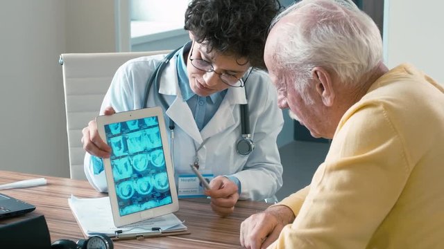 Female doctor showing results of MRI scan on tablet computer to retired patient