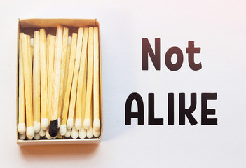 White matches and one match of black color in a box. Difference, self respect and acceptance concept. Motivational phrase on the image. Opposition, uniqueness, individualism concept. Not alike.