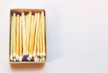 White matches and one match of purple color in a box. Self respect and yourself acceptance concept. Copyspace on the right side of the image for designers. Uniqueness and black sheep concept.