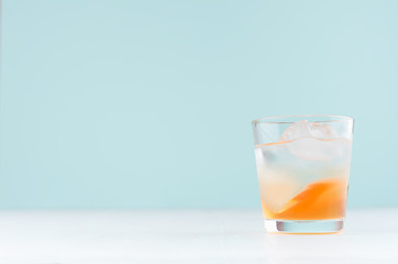 Refreshing oranges shot drink with ice cubes, liquor on soft light pastel green background, copy space.