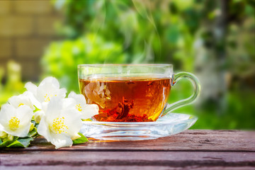Glass cup with tea and jasmine twig on wooden table, on blurred background