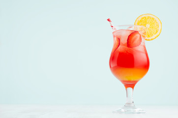 Tropical sunrise striped red, yellow drink with orange, strawberry piece, ice, straw in misted...