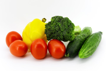 Variety of fresh vegetables on white background: plum-shaped red tomatoes, big yellow pepper, two large cucumbers, broccoli cabbage