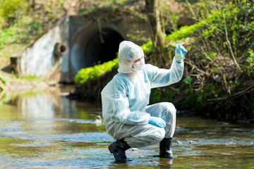 a scientist with a test tube takes a sample of water from a sewer discharge