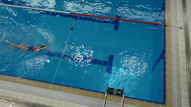 Female swimmer doing backstroke and flip turn in swimming pool with blue water, Top view