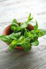 Bowl with fresh green mint on light wooden background