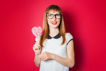 Young woman with a smile holds a lidien in the shape of a heart on a dark red background. Concept love, candy, confectionery
