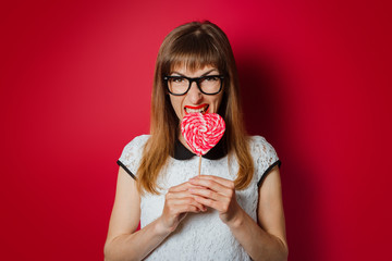 Young woman with a smile holds a lidien in the shape of a heart on a dark red background. Concept love, candy, confectionery