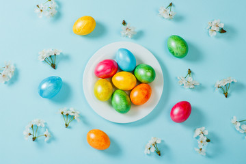 Easter eggs on a plate and spring flowers on a blue background background. Concept of celebrating Easter. Flat lay, top view