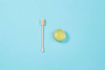 Jar of fresh honey and a wooden dipper on a blue background. Flat lay, top view