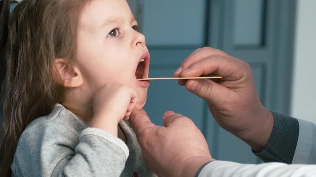 Little girl visiting doctor who watching her throat, with her mother