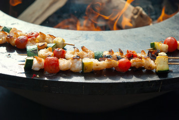 Peeled prawns and vegetables on grilled skewers