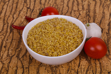 Raw bulgur in the bowl with tomatoes and garlic