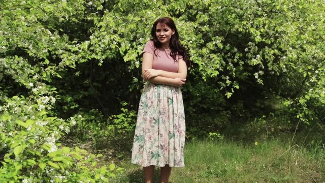 young brunette girl in dress posing in front of blooming garden, blooming Apple trees, summer, spring, beautiful nature