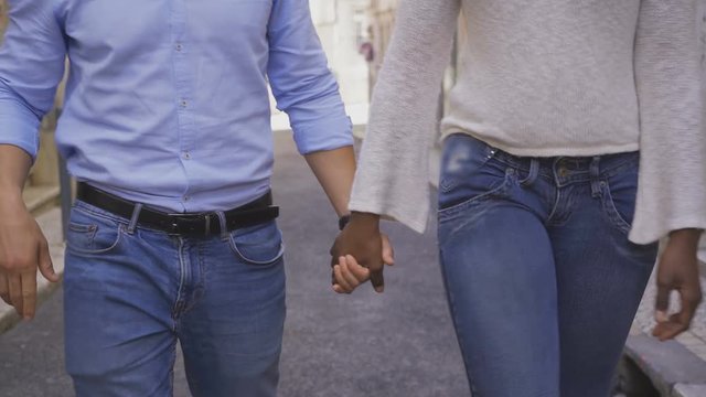 Cropped shot of multiracial couple holding hands together. Young African American woman and Caucasian man holding hands while walking on street. Relationship and dating concept